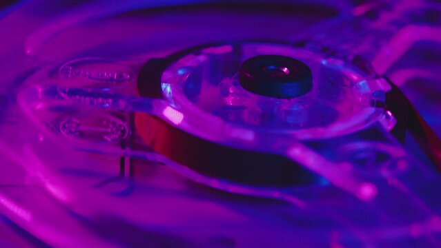 Close-up of a transparent reel rotating on a vintage analog tape recorder. Bobbin with retro tape in the light of the club violet-pink lights
