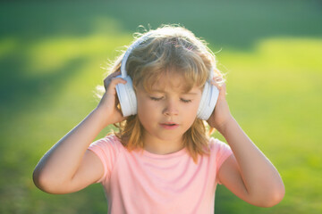 Child enjoy listens to music in headphones dreaming and relaxing. Stylish teen boy listening music in headphones and singing against green grass summer background.