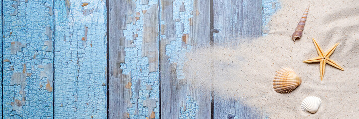 Summer, beach and vacation concept with free text space. Top view. Flat layout as wide banner format with various sea shells and fine beach sand on blue old wooden boards background