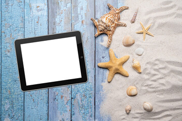 Summer, beach and vacation concept with free text space. Top view. A blank tablet, large sea star and sea shell and various sea shells and fine beach sand on an old blue wooden boards background
