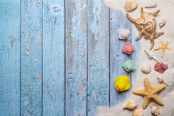 Summer, beach and vacation concept with free text space. Top view. Small group of colorful rubber ducks and various sea shells and fine beach sand on an old blue wooden boards background