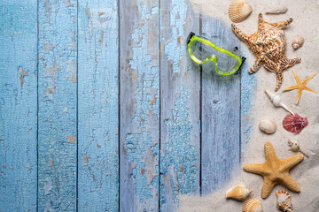 Summer, beach and vacation concept with free text space. Top view. Flat layout with a green diving goggles and various sea shells and fine beach sand on an old blue wooden boards background