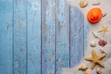 Summer, beach and vacation concept with free text space. Top view. Orange color rubber duck and various sea shells and fine beach sand on an old blue wooden boards background.