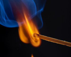 A glowing red match burns on a dark background, surrounded by fine wisps of smoke. Heat and flames...