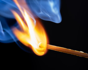 A glowing red match burns on a dark background, surrounded by fine wisps of smoke. Heat and flames...