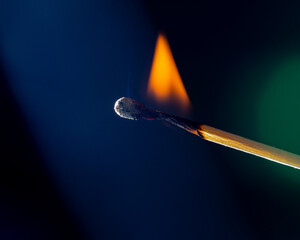 A glowing red match burns on a dark background, surrounded by fine wisps of smoke. Heat and flames...
