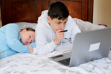 teenagers sit at computers do homework online study and are not tired of studying go to bed fall asleep One works the other sleeps no desire to study eyes hurt need to rest