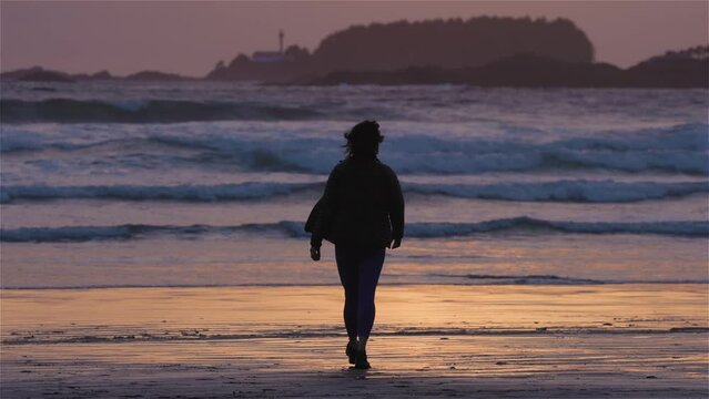 Adventurous Woman Standing on the Sandy Beach on the West Coast of Pacific Ocean. Cox Bay in Tofino, Vancouver Island, BC, Canada. Adventure Travel. Slow Motion.