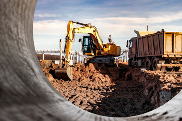 A wheeled excavator loads a dump truck with soil and sand. An excavator with a high-raised bucket against a cloudy sky View from the trench. Removal of soil from a construction site or quarry.