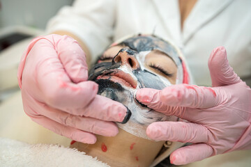 hands of a cosmetologist massage a face on which a mask is applied
