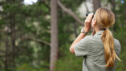 Binoculars, forest and woman explore in nature, travel journey or outdoor adventure for carbon footprint research. Watch, search and back person birdwatching in jungle, woods or eco green environment