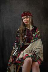 young Ukrainian lady in an embroidered blouse and a shawl poses against a dark background