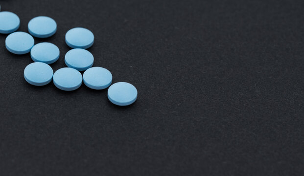 Heap of blue pills on a black table.