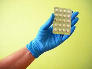 Hand holding pills in blister on green background,