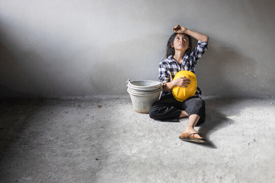Exhausted little girl sitting on floor concrete wall background. child labor and exploitation