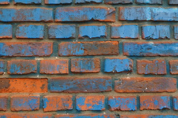 Closeup of weathered red brick wall with traces of blue paint. Speckled blue and orange textured...