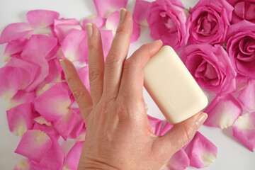organic soap bar in hand on roses and petal and white background, oil rose for natural cosmetic, top view