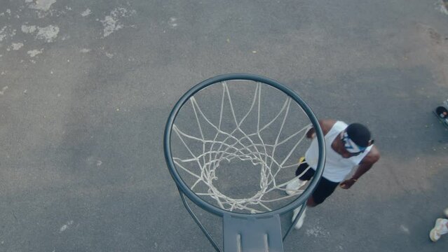 Young black man in sportswear playing basketball with friend on outdoor court, shooting a ball through the hoop. Top down shot