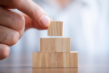 Close-up photo of putting wooden block on top of pyramid. Planning business growth. Horizontal concept with copy space for your text.