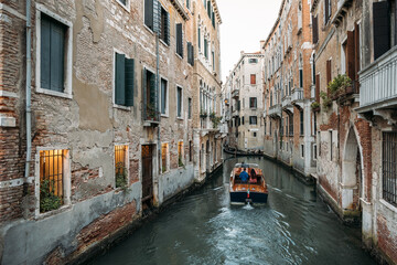 Fototapeta na wymiar A boat sailing through the narrow canals of Venice between ancient stone houses. The concept of a unique European city in Italy