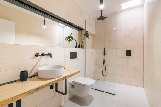 Bright stylish spacious bathroom with a round sink on a wooden countertop, a toilet and a shower. The concept of new housing or renovation in an old apartment