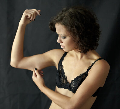 Anorexia, bulimia and woman checking her arm in studio for weight, obsession and depression on black background. Eating disorder, mental illness and girl suffering anxiety, body dysmorphia or disgust