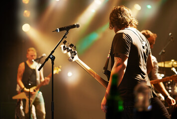 Performance, musician and men in a band at a concert for a music festival, event or show together. Night, stage and a group of people performing, singing and playing instruments at a club for a party