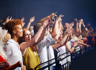 Crowd in fence row, fans at music festival or concert watching rock event on stage. Excited people in audience at band performance at arena, stadium or party with applause and energy at night show.