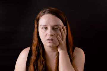 Tired young woman running hand down face. Female portrait isolated on black. Weakness and...
