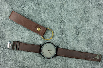 Leather key chain and leather wrist watch on a dark background. Top view