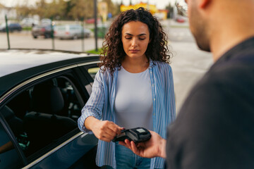 A young woman pays for fuel at a gas station using a card, the worker gave her a terminal to pay