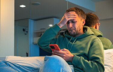 Man in trouble emotionally reacts to bad news that he read on phone or had fight over the call. Depressed guy at home with smartphone on bed.