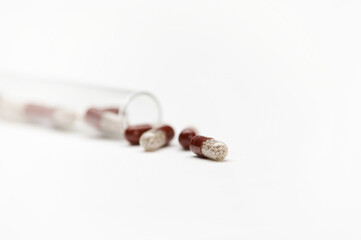 Still life with translucent gel capsules containing enteric granules, for treating diseases, scattering from laboratory test tube, isolated on white background. Pharmacy. Clinical research. Copy space