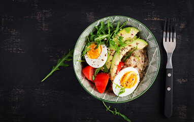 Breakfast oatmeal porridge with boiled eggs, avocado, tomatoes and green herbs. Healthy balanced food. Top view, flat lay
