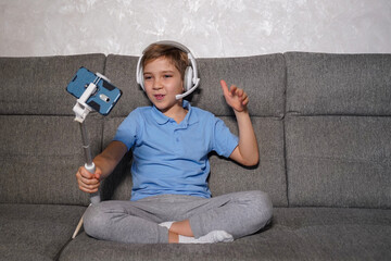 A teenager sits on the couch and talks on the phone on a selfie stick.