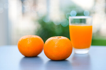 Fresh beautiful oranges and there is a cup of orange  juice place behind ,place on dark blue table with blur nature background and bokeh