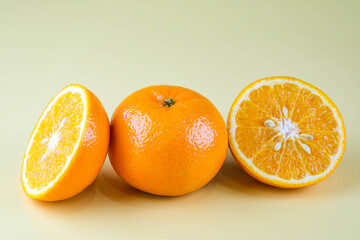 Fresh oranges and oranges cut in half isolated on soft yellow background