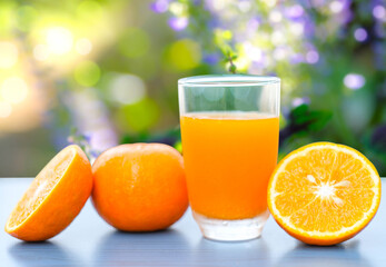 Fresh oranges juice and there are oranges beside ,place on dark blue table with blur beautiful nature flower and bokeh in the background