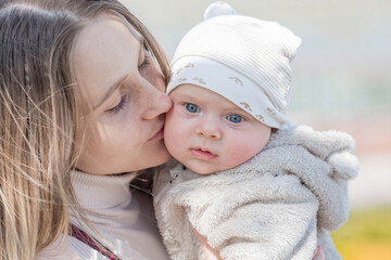 A young mother holds a charming little son in her arms. The kid looks at the camera and smiles. Portrait of a beautiful chubby 4-month-old baby.