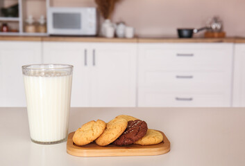 Board with cookies and glass of milk on dining table in kitchen