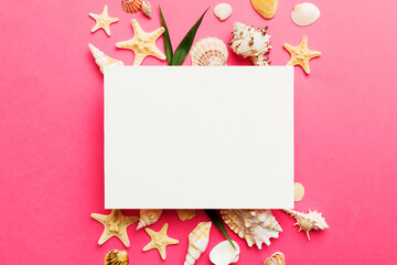 Summer time concept with blank greeting card and blank white paper on colored background. Seashells from ocean shore in the shape of frame separated with space for text top view