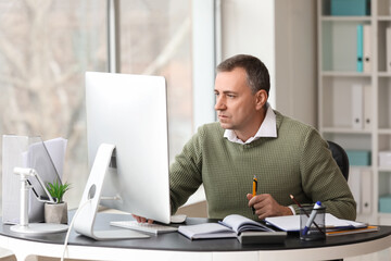 Fototapeta premium Mature accountant working with computer at table in office