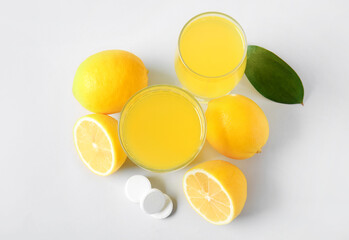 Glass of vitamin C effervescent tablet dissolved in water and lemons on grey background