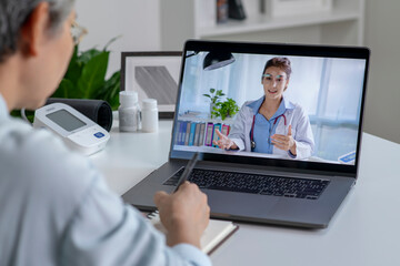 Asian woman with laptop during an online consultation with her doctor in her living room, telemedicine concept - 596594917