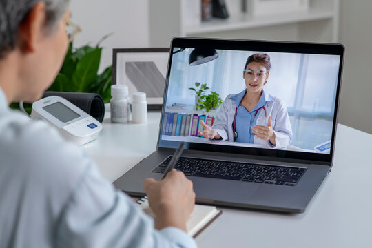 Asian woman with laptop during an online consultation with her doctor in her living room, telemedicine concept