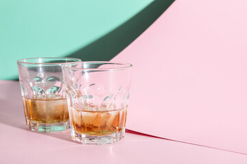 Glasses of rum with ice cubes on colorful background