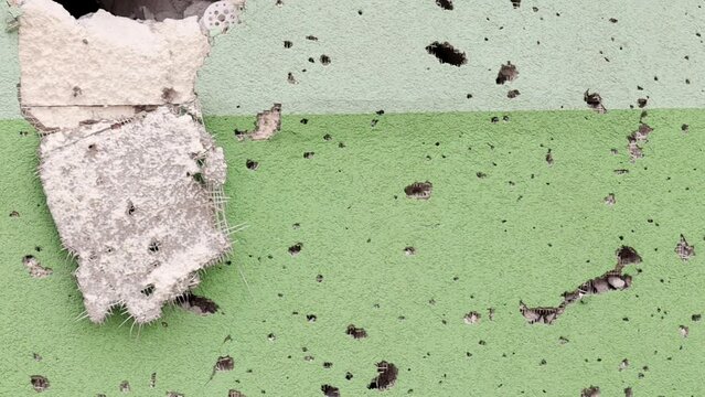 Holes from bullets and shrapnel in the wall on the front line. Scars of war. Concrete wall of a residential building with potholes and holes from gunfire. Consequences of the war in Ukraine.