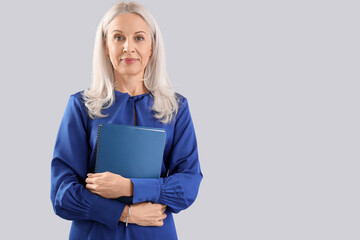 Mature woman with notebook on grey background