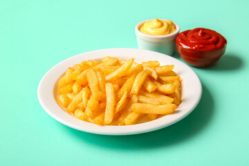 Plate of tasty french fries and sauces on color background