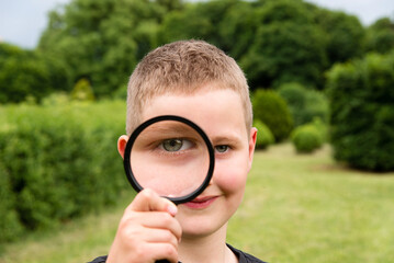 Cheerful boy looking through magnifying glass. Young biologist. Games in the park in summer. Family Day, Children's Day.